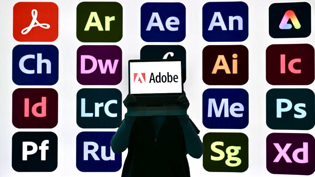  Somebody holding a laptop with the Adobe logo showing on its display in front of icons of different software applications. 