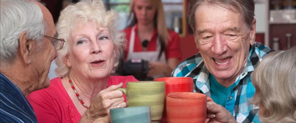 Group of four happy seniors with mugs toasting