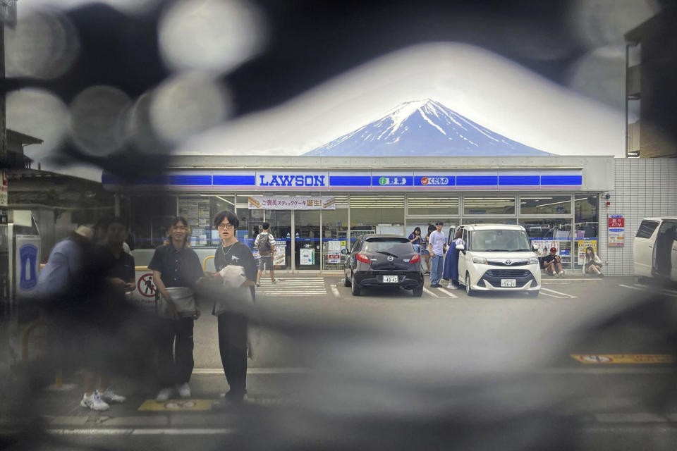 Mt. Fuji is seen through a hole on a black screen installed across from a convenience store in Fujikawaguchiko town, Yamanashi prefecture, central Japan on May 24, 2024. The town that erected the huge black screen last week in an attempt to stop tourists from snapping photos of Mount Fuji and overcrowding the area has discovered holes in the screen and is working to repair them, officials said Tuesday. (Kyodo News via AP)