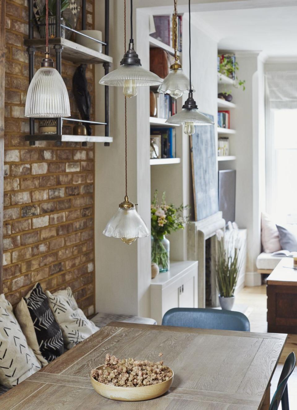 antique glass pendant lights hang above a wooden dining table against a background of exposed brickwork