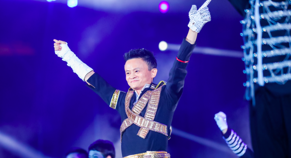 Alibaba founder Jack Ma holds his hands up in victory on stage at an event.