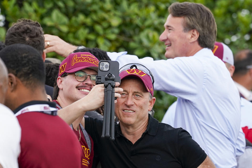 Washington Commanders owner Josh Harris takes selfie with a fan, as Virginia Gov. Glenn Youngkin, right, greets fans before a NFL football practice at the team's training facility, Thursday, July 27, 2023 in Ashburn, Va. (AP Photo/Alex Brandon)