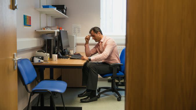 A doctor sits at his desk looking very worried.