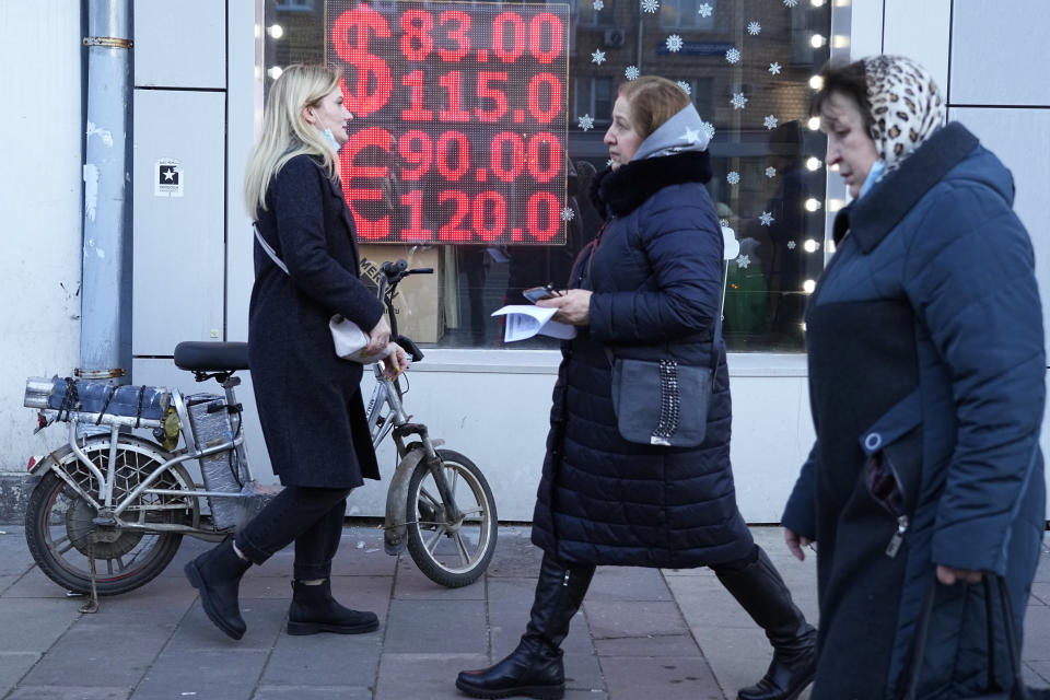 People walk past a currency exchange office screen displaying the exchange rates of U.S. Dollar and Euro to Russian Rubles in Moscow's downtown, Russia, Monday, Feb. 28, 2022. Ordinary Russians are facing the prospect of higher prices as Western sanctions over the invasion of Ukraine sent the ruble plummeting. That's led uneasy people to line up at banks and ATMs on Monday in a country that has seen more than one currency disaster in the post-Soviet era. (AP Photo/Pavel Golovkin)