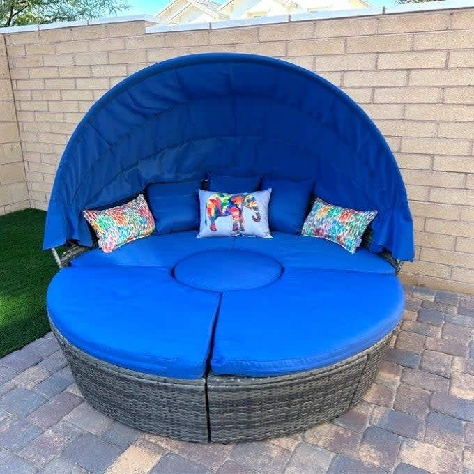 a reviewer photo of a round, blue outdoor lounge bed with cushions and a semicircular canopy against a wall