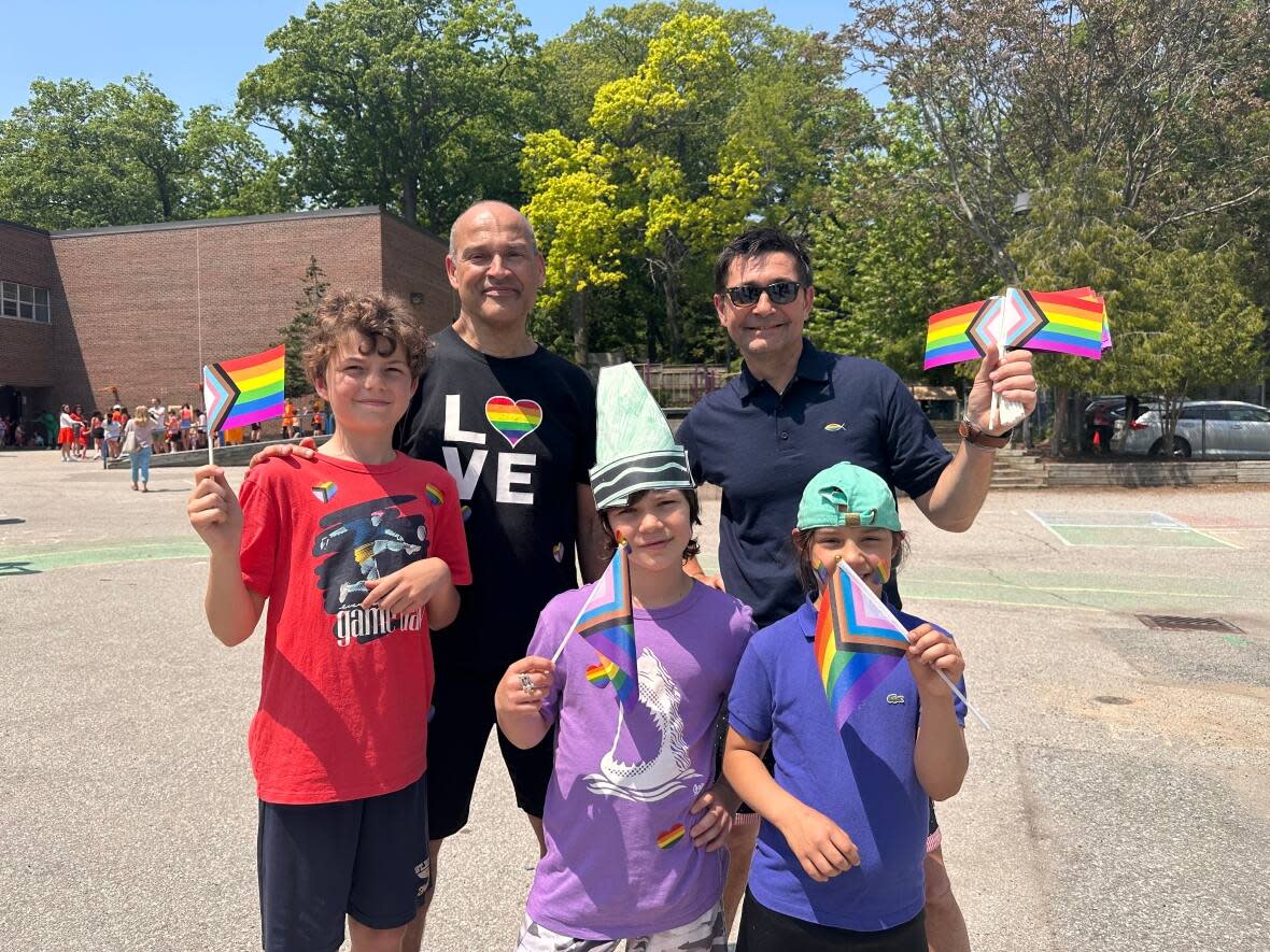 David Toto, back row left, and Laurent Papaix, back row right, and their three children wave Progress Pride flags at a special celebration at St. Denis Catholic School on Wednesday in Toronto. (Talia Ricci/CBC - image credit)