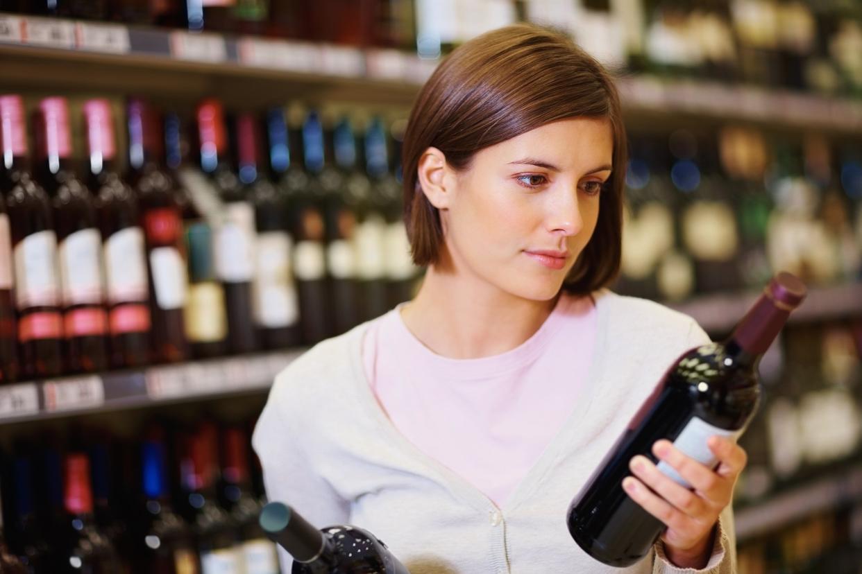 young woman selecting wine bottle at supermarket