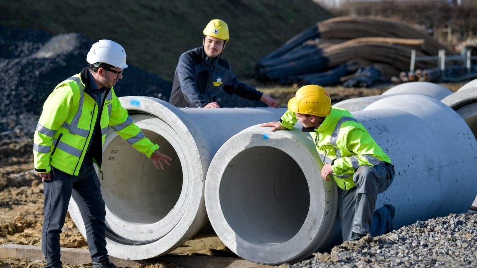 Shenadi Osmani bespricht mit den angehenden Kanalbauern Issam Bhihi und Steffen Hallermann die Kontrolle der Dichtungen von Betonrohren auf einer Baustelle.