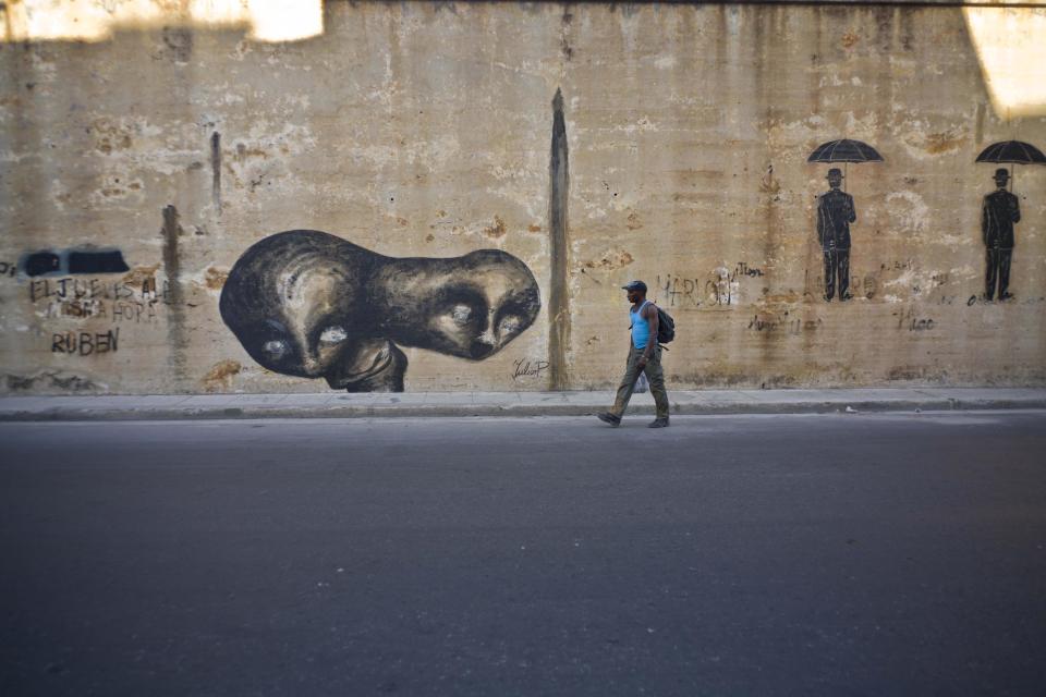 In this Feb. 12, 2017 photo, a pedestrian walks past street art by urban artist Yulier P. adorning a wall on a street in Havana, Cuba. "It is important to me that the urban artist express himself freely, not restricted by anyone, not a gallery, not a government," said the 27-year-old artist, whose full name is Yulier Rodríguez Pérez. (AP Photo/Ramon Espinosa)