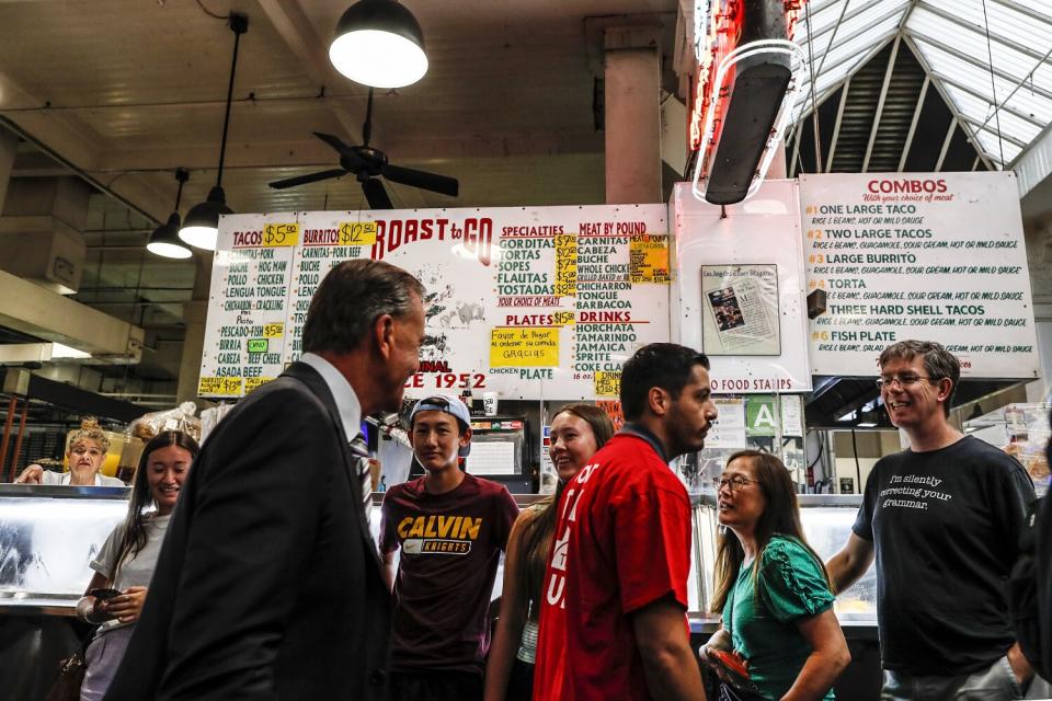 A man in a suit walks by more casually dressed people in front of a food stall.