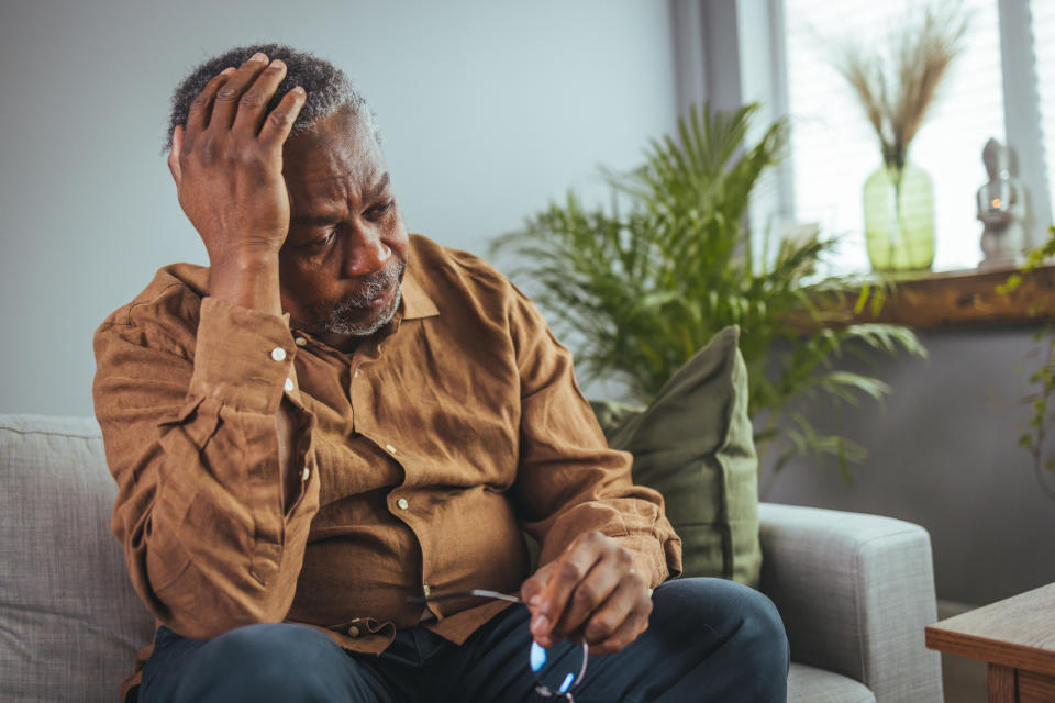 Elderly man sitting, looking worriedly with a pair of glasses in his hand