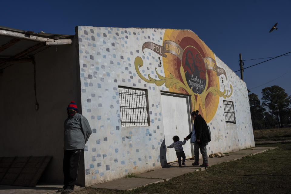 A childcare worker and her charge walk past a building housing a study center run by the Frente de Organizaciones en Lucha, FOL, social organization in the "El Peligro" neighborhood, south of Buenos Aires, Argentina, Friday, May 20, 2022. The social organization runs a soup kitchen along with a daycare center, vegetable garden, library and a study center for high school students in the impoverished neighborhood. (AP Photo/Rodrigo Abd)