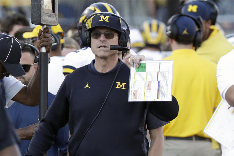 Jim Harbaugh paces the sideline holding a play card.