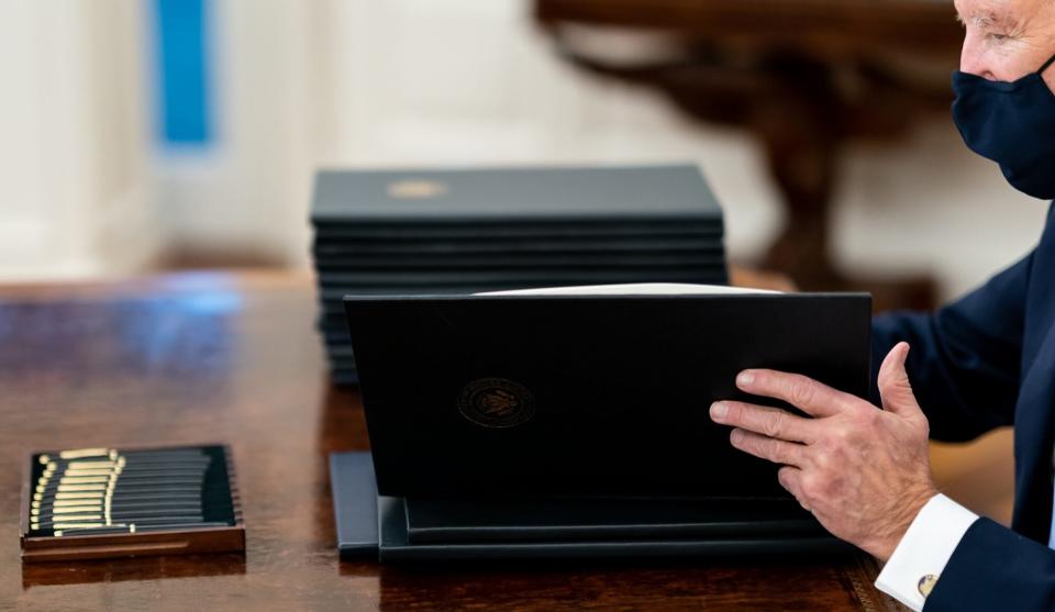 President Joe Biden opens one of several executives orders that that he will sign Wednesday, Jan. 20, 2021, in the Oval Office of the White House.