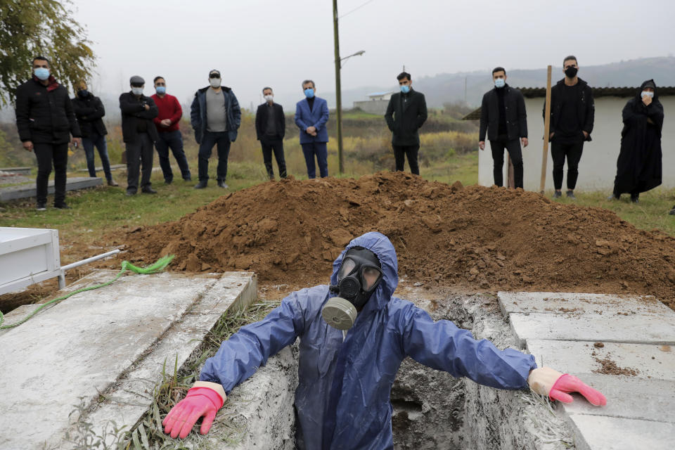 Mohammad Hossein Khoshnazar, 18, a cleric volunteer wearing protective clothing prepares a grave for a funeral of Mahmoud Yousefi, 72, who died from COVID-19 at a cemetery in the Raykandeh village on the outskirts of the city of Ghaemshahr, in northern Iran, Friday, Dec. 18, 2020. (AP Photo/Ebrahim Noroozi)