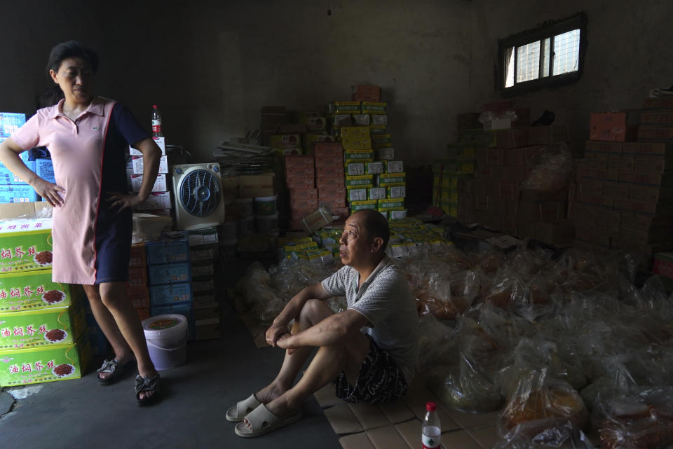 Yu Ruiping, left, and her husband Lu Jinlin, middle, rest in a family warehouse with pickled vegetables that they salvaged from the floods in Xinxiang in central China's Henan Province, Monday, July 26, 2021. Record rain in Xinxiang last week left the couple's goods in a nearby market underwater, causing losses that could run into the tens of thousands of dollars. Dozens of people died in the floods that immersed large swaths of central China's Henan province in water. (AP Photo/Dake Kang)