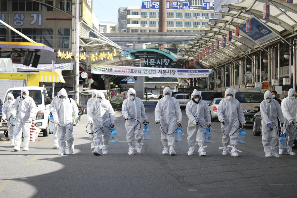 Trabajadores en trajes protectores rocían desinfectante para prevenir contagios con el coronavirus que produce la enfermedad COVID-19, en un mercado local de Daegu, Corea del Sur, el domingo 23 de febrero de 2020. (Im Hwa-young/Yonhap vía AP)