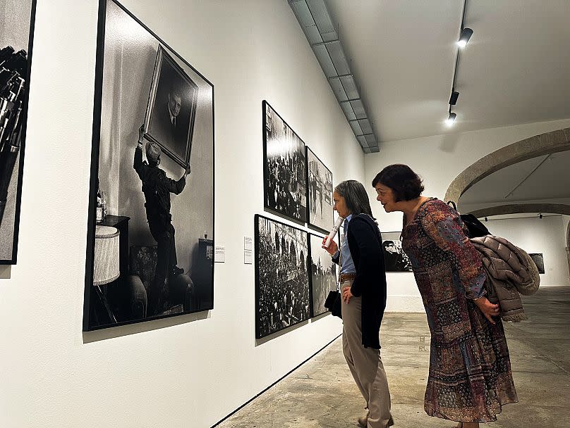 Two women contemplate the photo taken by Eduardo Gageiro, capturing the moment a soldier removes Salazar's portrait from the headquarters of the State police.