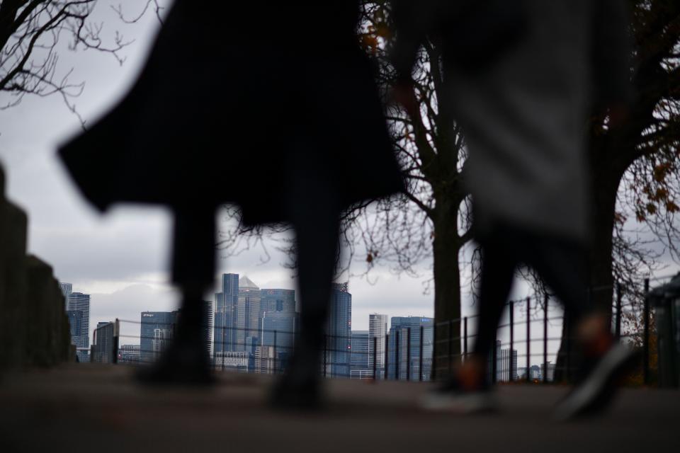 People walk in Greenwich Park with the office buildings of the Canary Wharf financial district in the background  in London on November 25, 2020. - Britain's economy is set to shrink 11.3 percent this year, suffering the greatest annual slump in more than three centuries on coronavirus fallout, the government forecast Wednesday. The economy is expected to rebound 5.5 percent next year and 6.6 percent in 2022, finance minister Rishi Sunak told parliament. (Photo by Ben STANSALL / AFP) (Photo by BEN STANSALL/AFP via Getty Images)