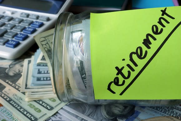 Jar holding cash with a green Post-It with the word retirement on it, on a desk with a calculator and more cash.