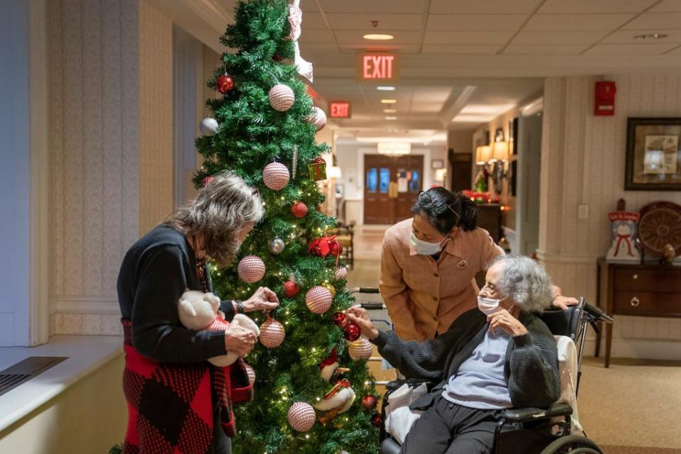 Tina Sandri, CEO of Forest Hills of DC senior living facility, center, greets residents Cherie Neville, left, and Catherine Doleman on Thursday, Dec. 8, 2022, in Washington. As nursing home leaders redouble efforts to get staff and residents boosted with the new vaccine version, now recommended for those 6 months and older, they face complacency, misinformation and COVID-19 fatigue.