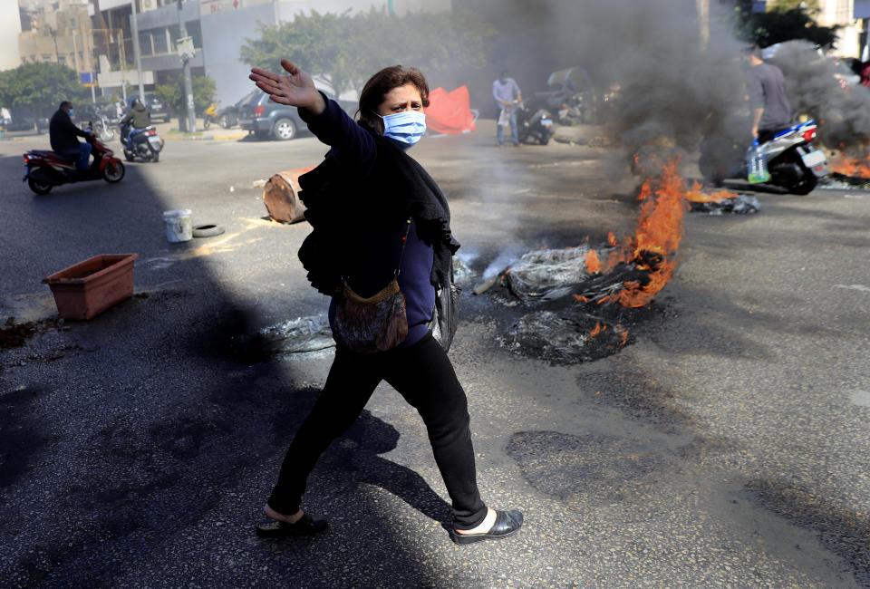 A Lebanese woman shouts slogans against Lebanese politicians, as she passes in front of burning tires to block a main road, during a protest against the increase in prices of consumer goods and the crash of the local currency, in Beirut, Lebanon, Tuesday, March 16, 2021. Scattered protests broke out on Tuesday in different parts of the country after the Lebanese pound hit a new record low against the dollar on the black market. (AP Photo/Hussein Malla)