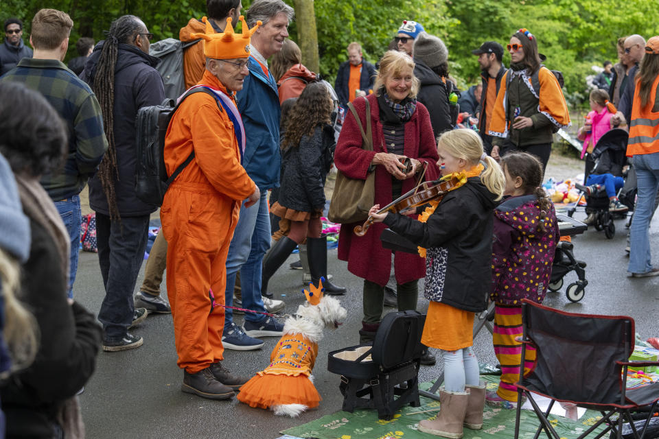 An orange-clad man and his orange-clad dog listen to a girl playing violin during King's Day celebrations in Amsterdam, Netherlands, Saturday, April 27, 2024. (AP Photo/Peter Dejong)