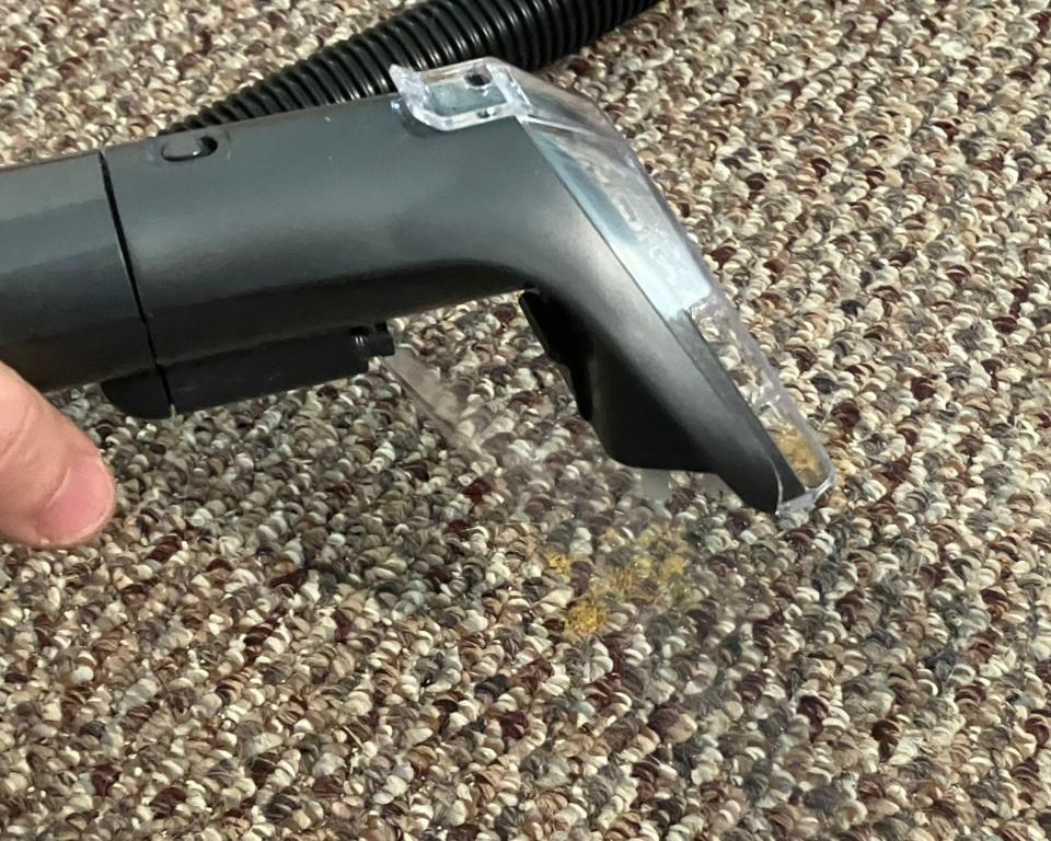 Spraying a low-pile beige carpet with yellow stain using the Bissell Little Green Portable Carpet Cleaner attachment