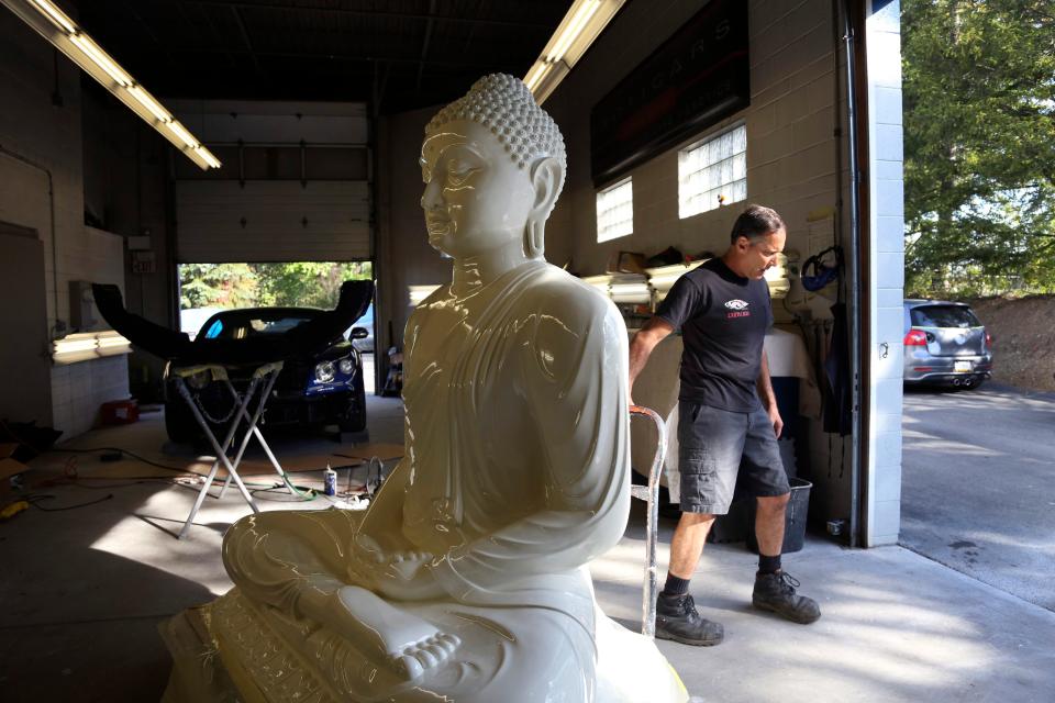 Dave Ley, co-owner of Exoticars, an auto restoration shop specializing in classic vehicles, pulls a restored statue of the Buddha outside his shop in McCandless, Pa.