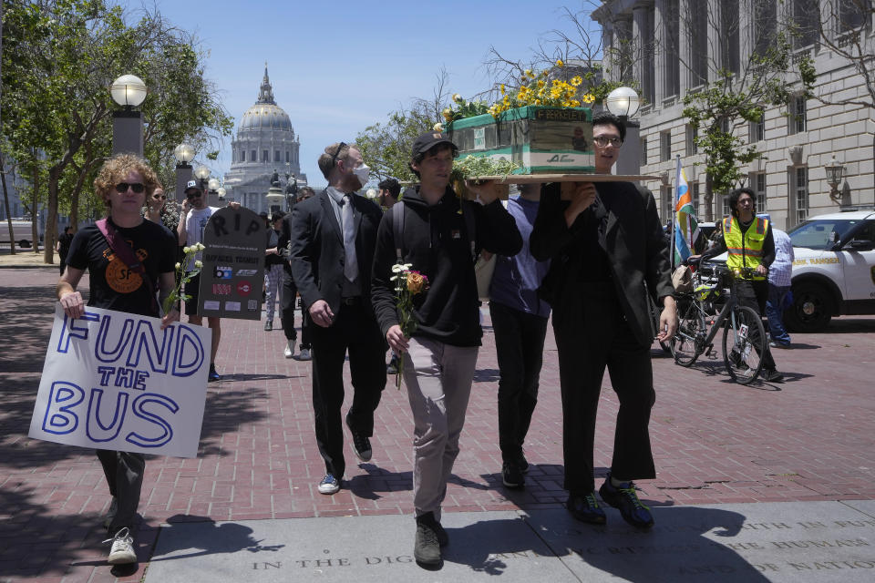 Protesters carry signs and a model of an AC Transit bus during a "funeral for public transit" march in San Francisco, Saturday, June 3, 2023. California's public transit agencies say they are running out of money, plagued by depleted ridership from the pandemic and soon-to-expire federal aid. But California's state government is having its own financial problems, leaving the fate of public transit agencies uncertain in this car-obsessed state. (AP Photo/Jeff Chiu)