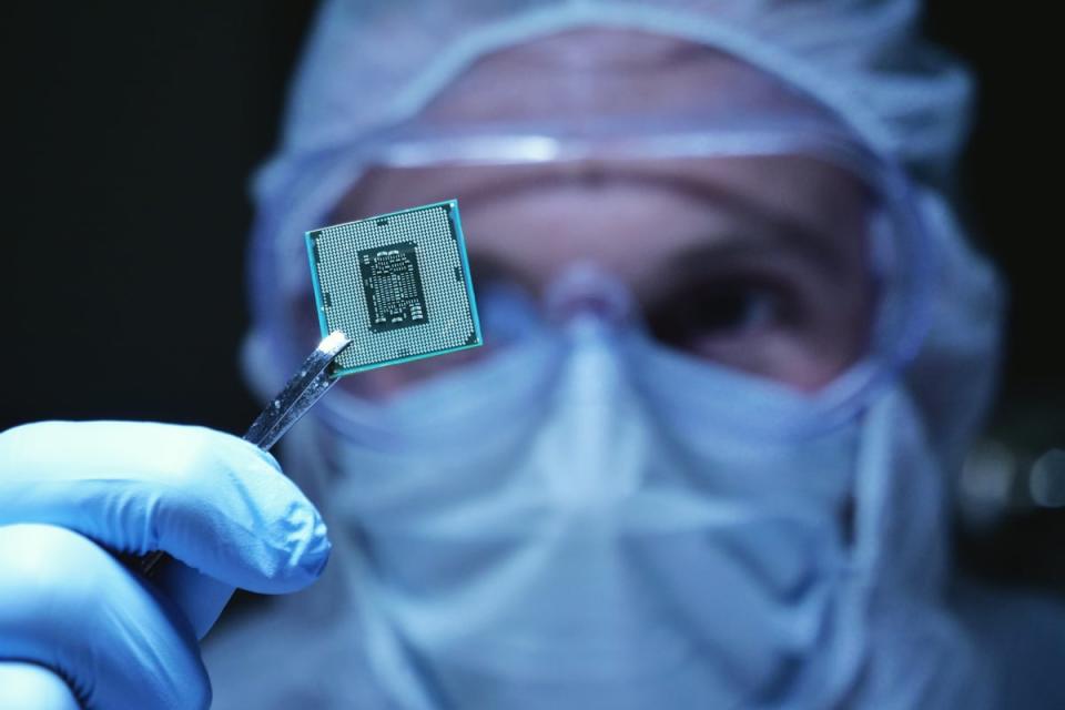 An engineer in a clean suit looking at a microchip held by tweezers.