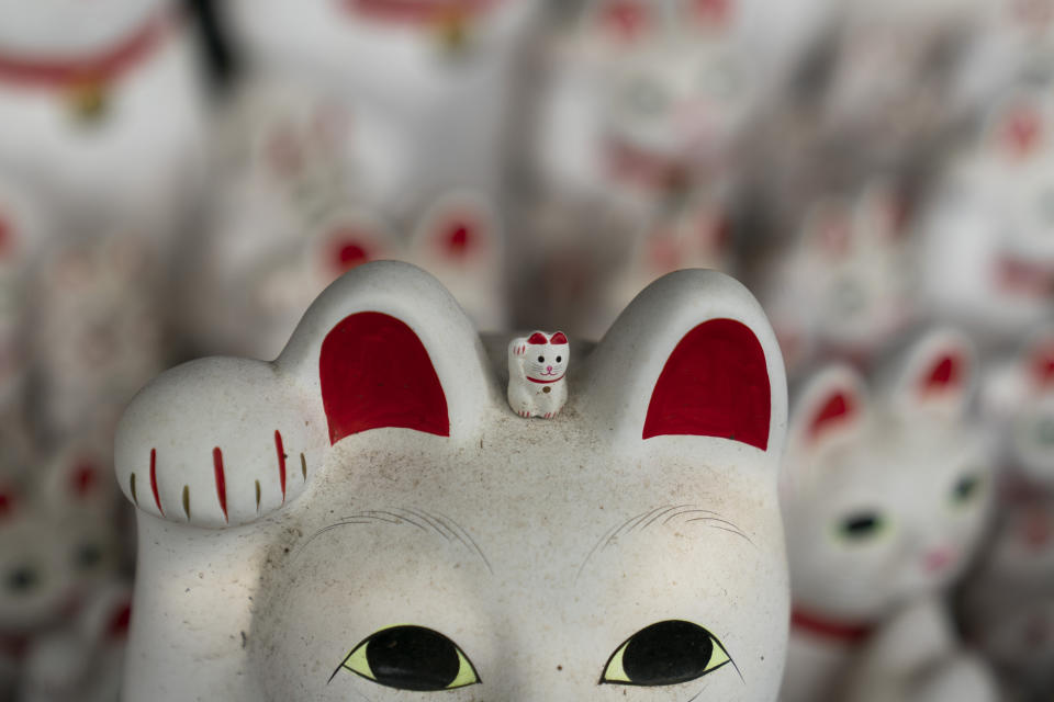 In this June 25, 2019, photo, a small beckoning cat figurine is place on top of a large statue at Gotokuji Temple in Tokyo. According to a centuries-old legend provided by the temple, Gotokuji, a Buddhist temple located in the quiet neighborhood of Setagaya, is the birthplace of beckoning cats, the famous cat figurines that are widely believed to bring good luck and prosperity to home and businesses. Some visitors come just to snap a few photos, while others make a trip to the temple to pray and make wishes. (AP Photo/Jae C. Hong)