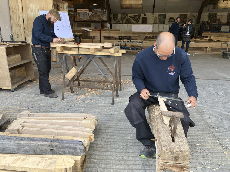 Carpenters work on pieces, part of the new roof for the Notre Dame de Paris cathedral, Thursday, May, 25, 2023, near Angers, western France. Carpenters building a new timber frame for the fire-ravaged roof of Paris' Notre Dame Cathedral are using the same tools and techniques as their medieval predecessors. For them, working with hand-axes to fashion oak beams has been like stepping back in time. (AP Photo/Jeffrey Schaeffer)