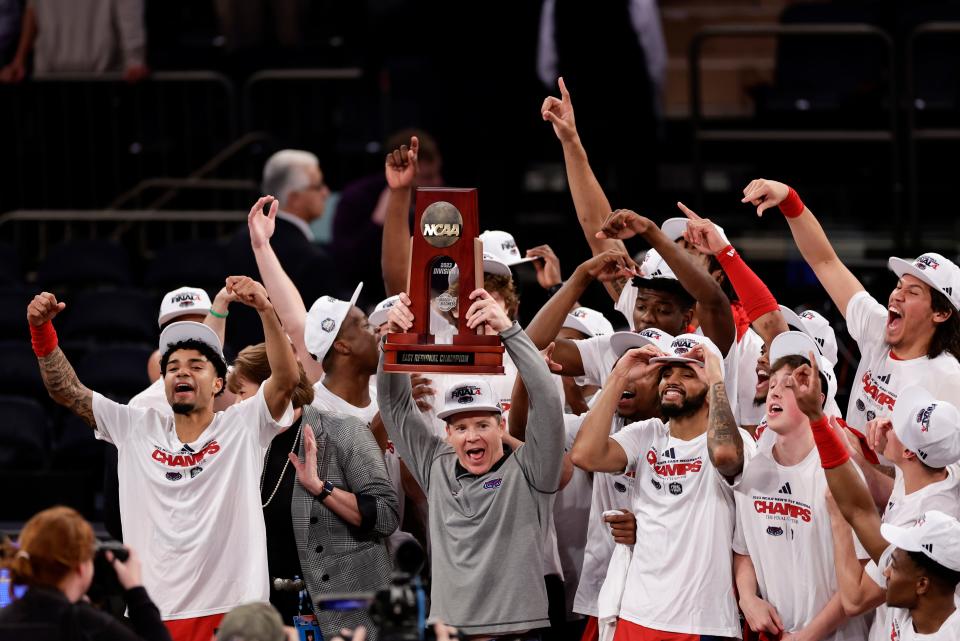 Florida Atlantic head coach Dusty May holds up the trophy as players celebrate their Elite Eight win over Kansas State.