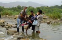 FILE - In this March 14, 2020 file photo, a Venezuelan woman is carried across a river to Colombia from Venezuela, near the Simon Bolivar International Bridge in La Parada near Cucuta, Colombia. Colombian President Ivan Duque ordered the nation's border with Venezuela closed as a coronavirus containment measure. (AP Photo/Antonio Ospina, File)