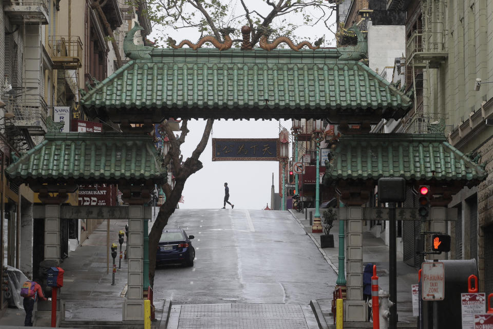 A pedestrian crosses Grant Street behind the Dragon Gate, an entrance to Chinatown in San Francisco, Saturday, April 4, 2020. The new coronavirus causes mild or moderate symptoms for most people, but for some, especially older adults and people with existing health problems, it can cause more severe illness or death. (AP Photo/Jeff Chiu)