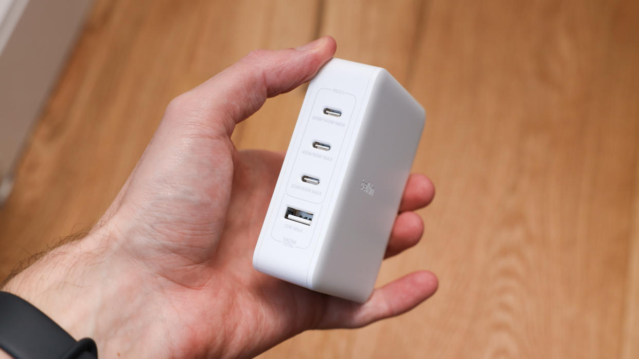  Belkin BoostCharge Pro 140W 4-Port GaN Wall Charger held in a hand above a wooden floor. 