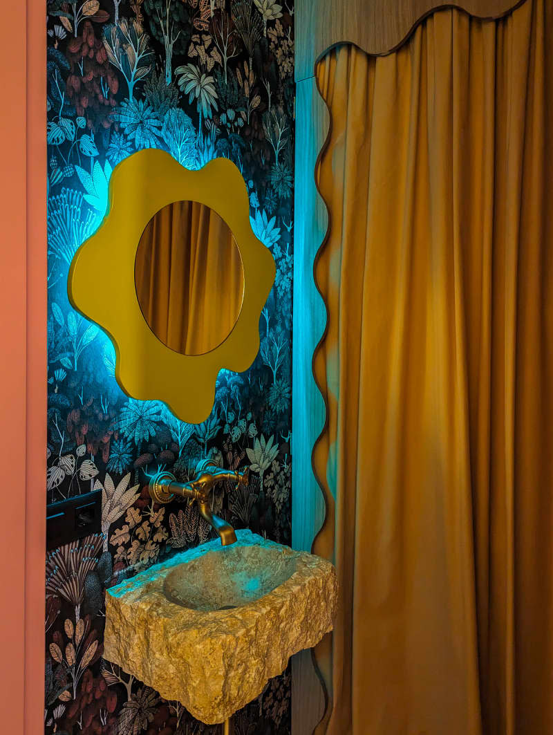 Bathroom with navy botanical wallpaper, yellow wavy mirror, and gold curtain