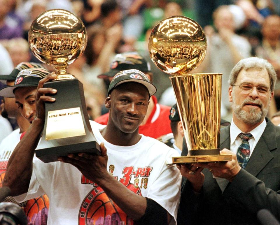 (FILES) In this 14 June 1998 file photo, Michael Jordan (L) holds the NBA Finals Most Valuable Player trophy and former Chicago Bulls head coach Phil Jackson holds the NBA champions Larry O'Brian trophy 14 June after winning game six of the NBA Finals with the Utah Jazz at the Delta Center in Salt Lake City, UT. The Bulls won the game 87-86 to take their sixth NBA championship. Jackson left the Bulls following the 1998 season and 12 January reports indicate that Jordan plans to announce his retirement at a 13 January news conference in Chicago.   AFP PHOTO/FILES/Jeff HAYNES (Photo by JEFF HAYNES / AFP) (Photo by JEFF HAYNES/AFP via Getty Images)