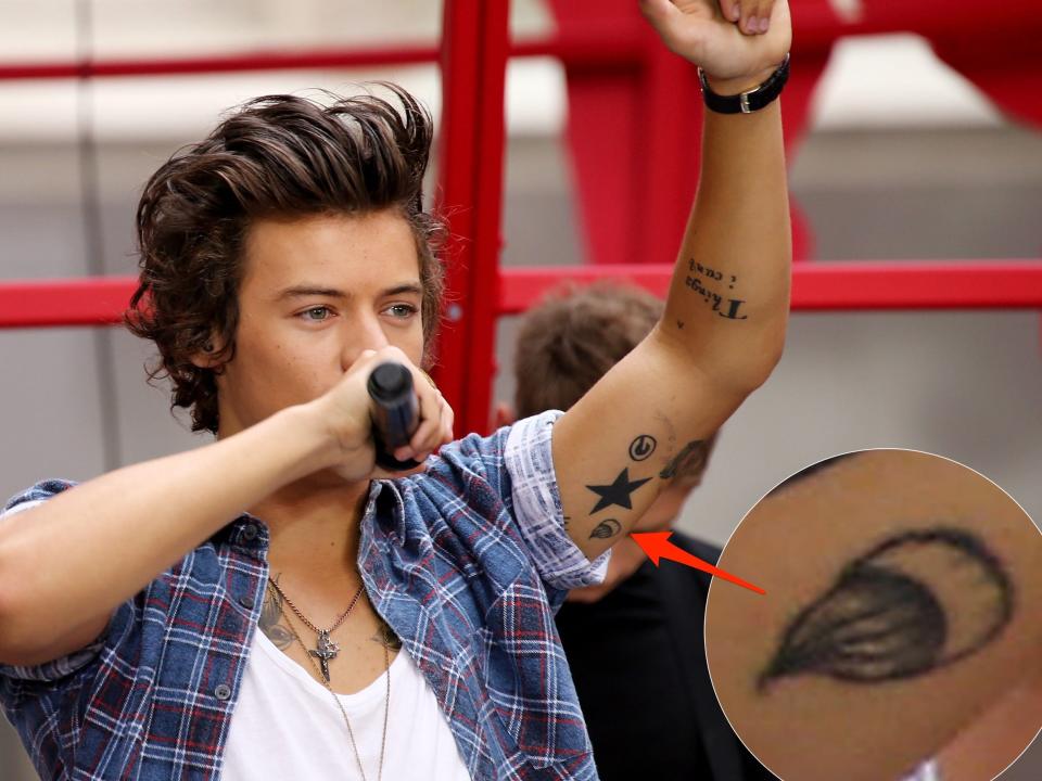 A red arrow pointing to a cookie tattoo on Harry Styles' left bicep.