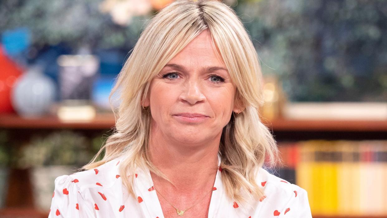 Zoe Ball in a white shirt and jeans sitting on a sofa