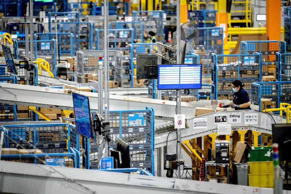 Workers amid yellow and blue machinery and conveyor belts sorting packages in a large warehouse.