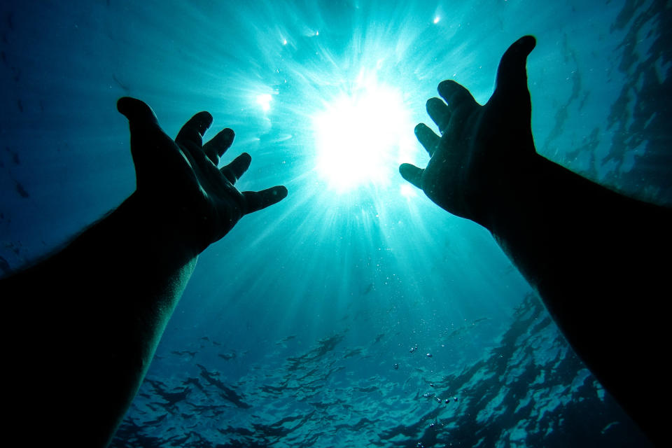 Two hands reaching for the surface under water