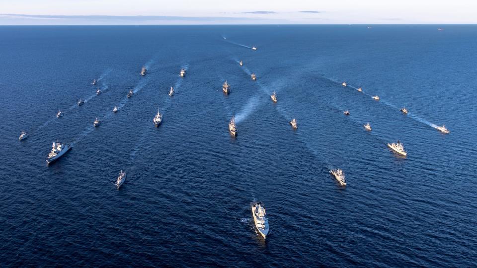 Various NATO warships sail in columns in the blue water of the Baltic Sea.