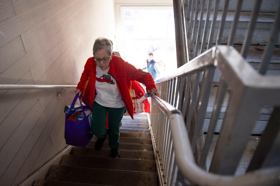 Janice Woods, YMCA volunteer, carries a bag of food up the stairs at Front Porch Housing to be delivered to a family for Christmas in Greenville on Friday, Dec. 15, 2023.