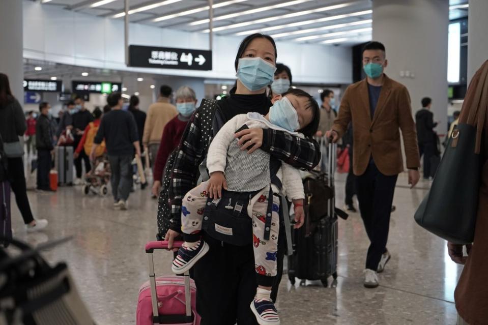 A mother with her child at a train station in Hong Kong, both wearing protective face masks.