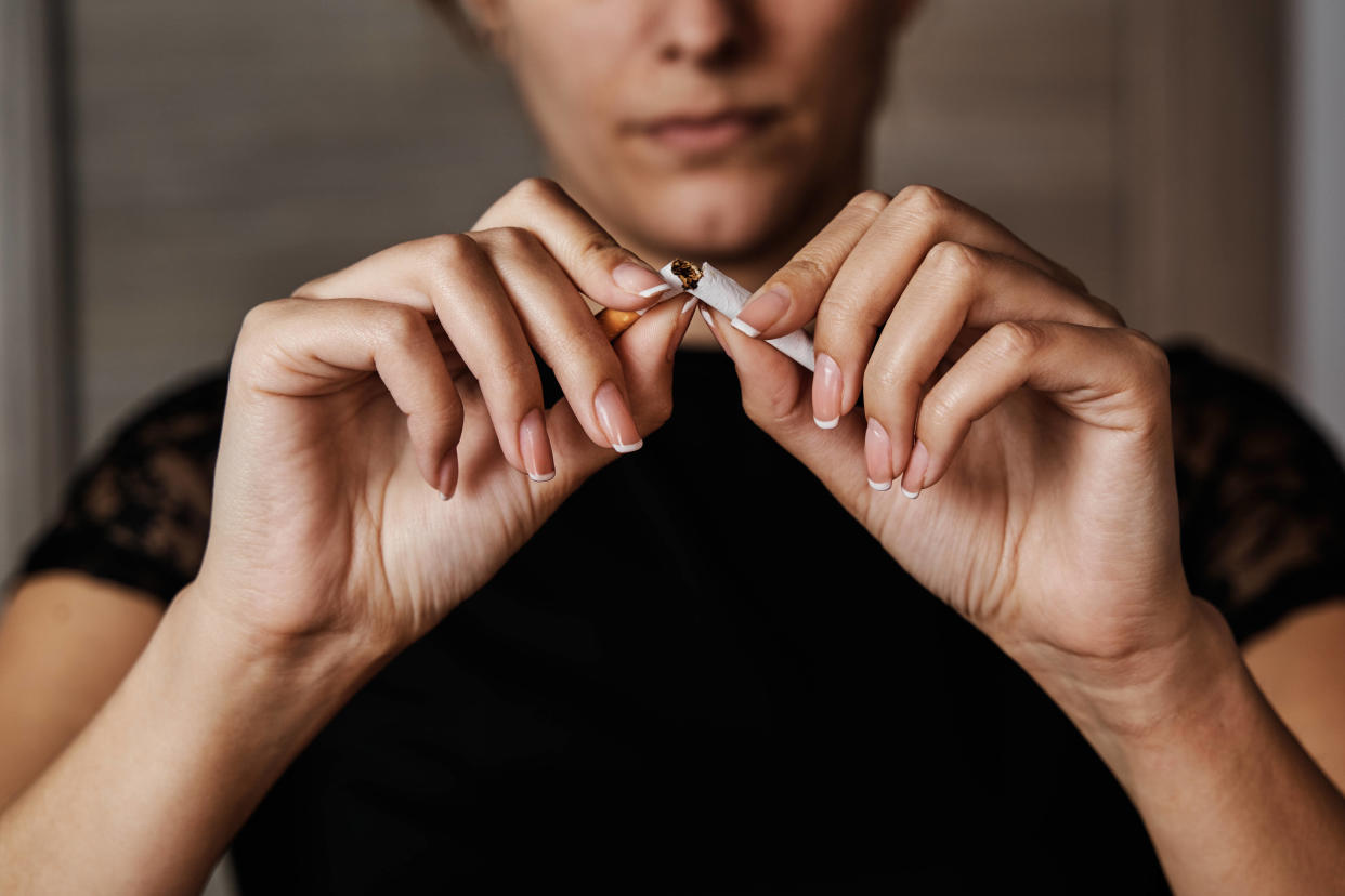 Unrecognizable young woman breaking a cigarette in half to stop smoking. Concept of smoking and addiction.