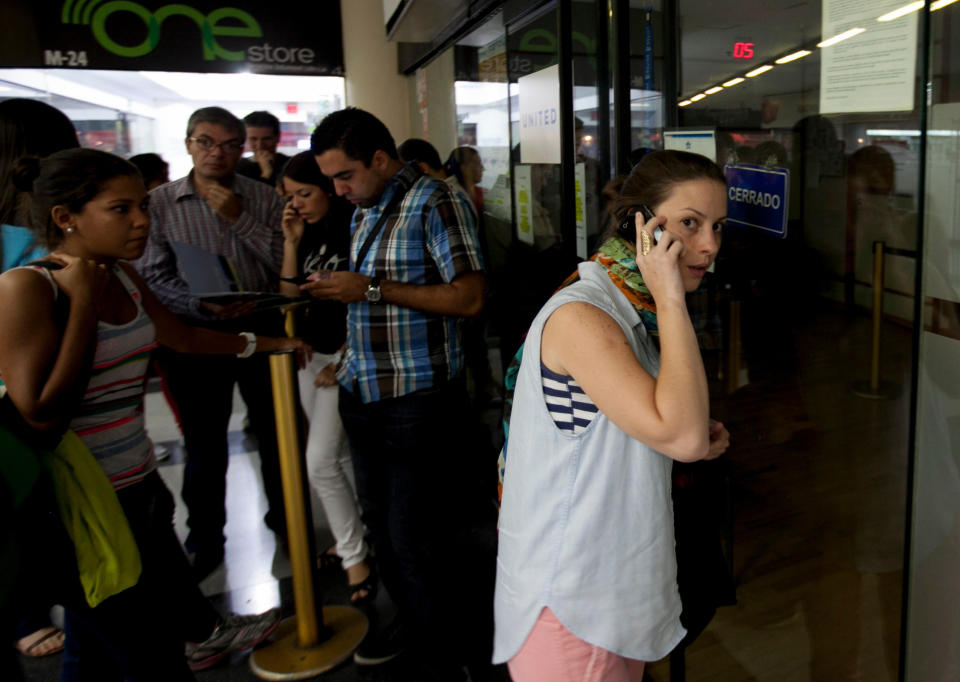 A woman speaks on her cell as she seeks information about flight sales from a closed United Airlines office in Caracas, Venezuela, Friday, Jan. 24, 2014. Delta, American Airlines and Panama's Copa Airlines were also among carriers whose offices were either closed or had halted sales on Friday after the government devalued the local currency for flights abroad. (AP Photo/Alejandro Cegarra)