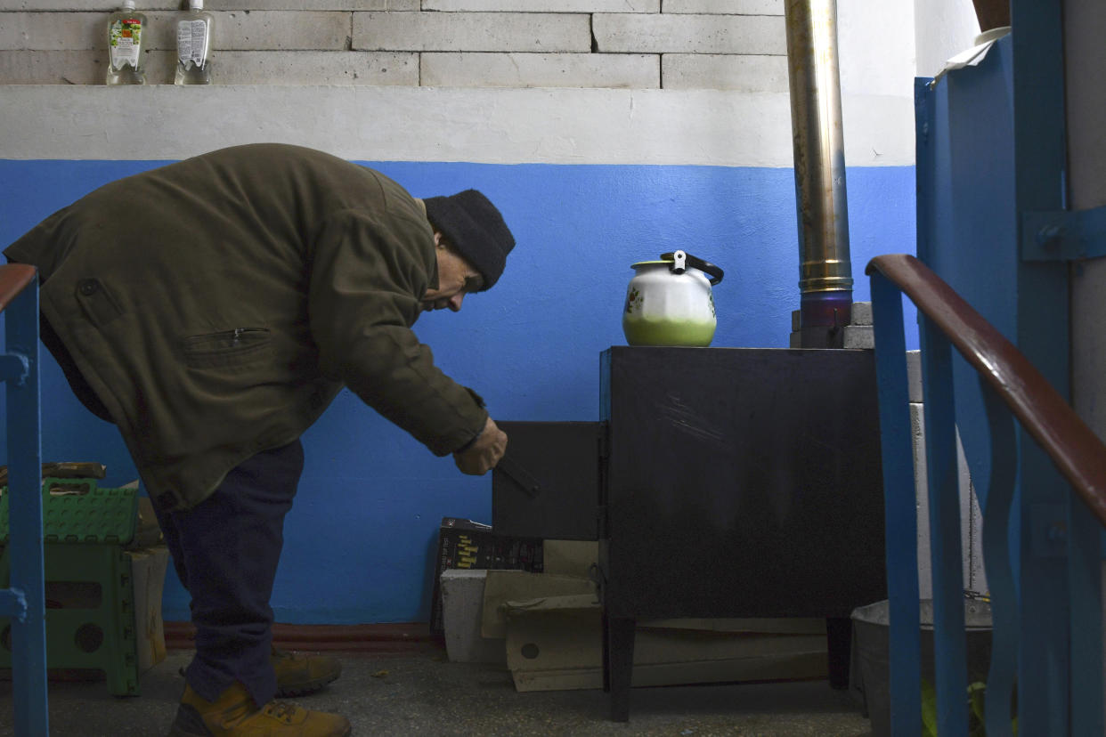 A man cooks food on a potbelly stove on the stairs entrance of an apartment building in Lyman, Donetsk region, Ukraine, Sunday, Nov. 20, 2022. The situation in Ukraine's capital, Kyiv, and other major cities has deteriorated drastically following the largest missile attack on the country's power grid on Tuesday, Nov. 15, 2022. Ukrainian state-owned grid operator Ukrenergo reported that 40% of Ukrainians were experiencing difficulties, due to damage to at least 15 major energy hubs across the country. (AP Photo/Andriy Andriyenko)