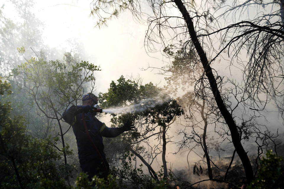 A firefighter extinguish the fire during a wildfire in Thea area some 60 kilometers (37 miles) northwest of Athens, Greece, Thursday, Aug. 19, 2021. A major wildfire northwest of the Greek capital devoured large tracts of pine forest for a third day and threatened a large village as hundreds of firefighters, assisted by water-dropping planes and helicopters, battled the flames Wednesday. (AP Photo/Thanassis Stavrakis)